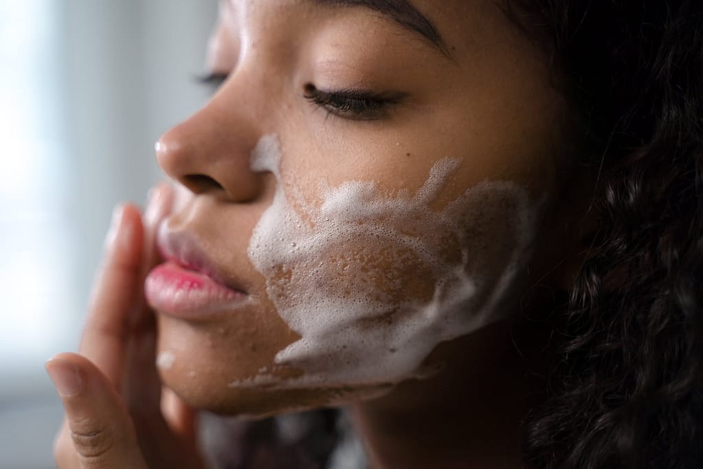 close up shot of a curly haired woman cleaning her face
