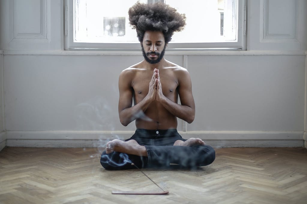 topless man in black denim jeans sitting on floor doing meditation